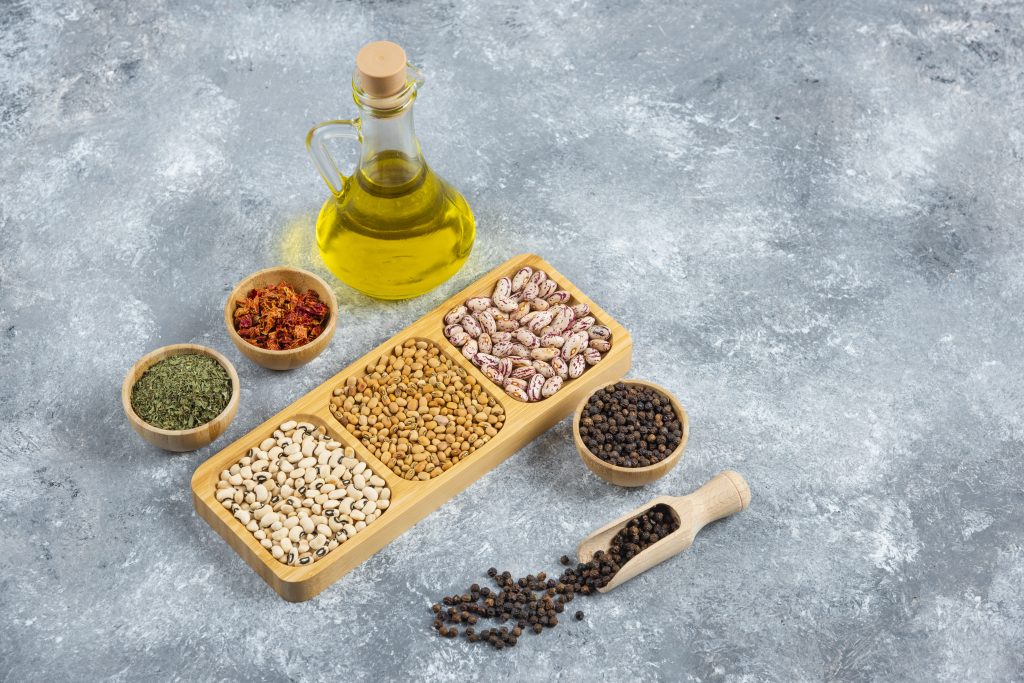 plates of raw beans and bottle of oil on marble background